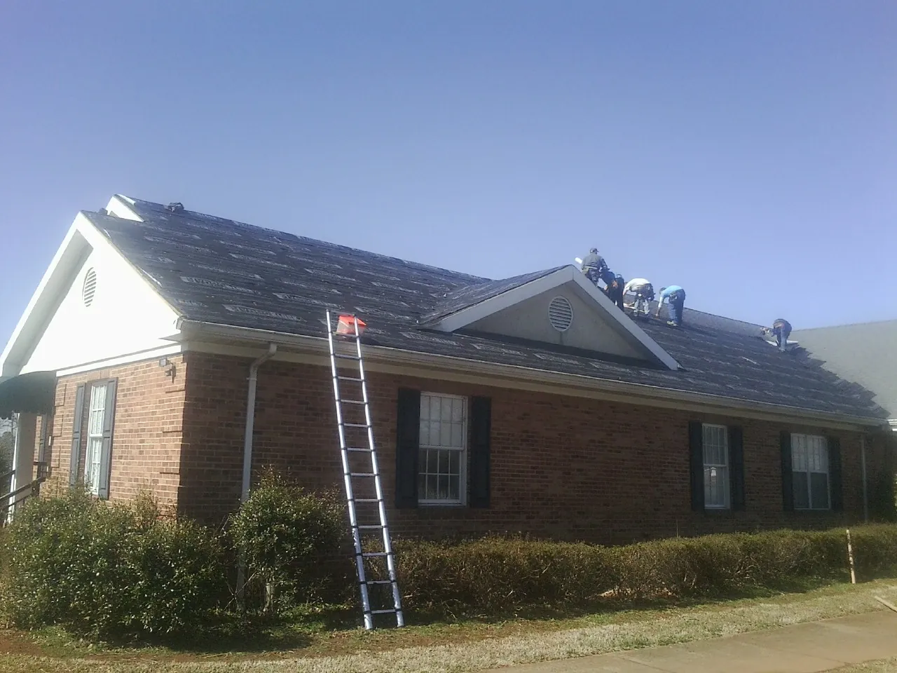 Crew tearing shingles off a brick ranch roof with a ladder set — Emergency Roof Repair work by our crew in Cantrall