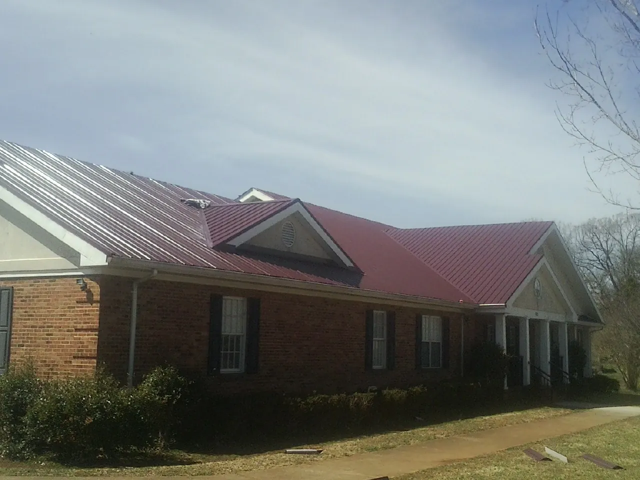 Red metal roof with gabled entries on a long brick building, from a Hail Damage Roof Repair job in Cantrall