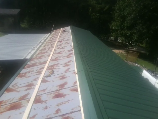 Old rusted panels beside newly installed green metal roofing — Wind Damage Roof Repair by Roofing Brothers in Cantrall