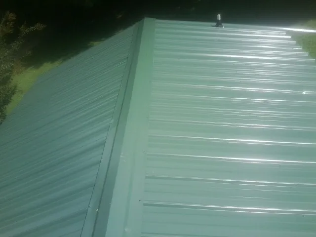 New green metal panels meeting at the ridge of a roof — Flat Roof Repair work by our crew in Cantrall