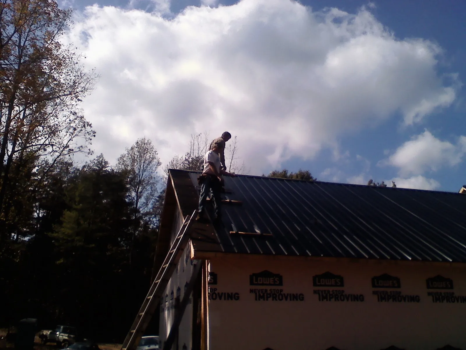 Roofer fastening dark metal panels high against a cloudy sky, from a Roof Inspection job in Cantrall