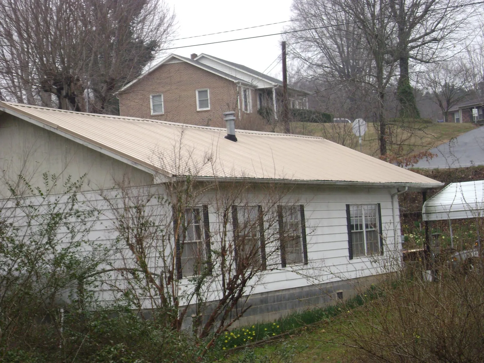 Tan metal roof on a white sided house set into a hillside — Commercial Roofing by Roofing Brothers in Cantrall