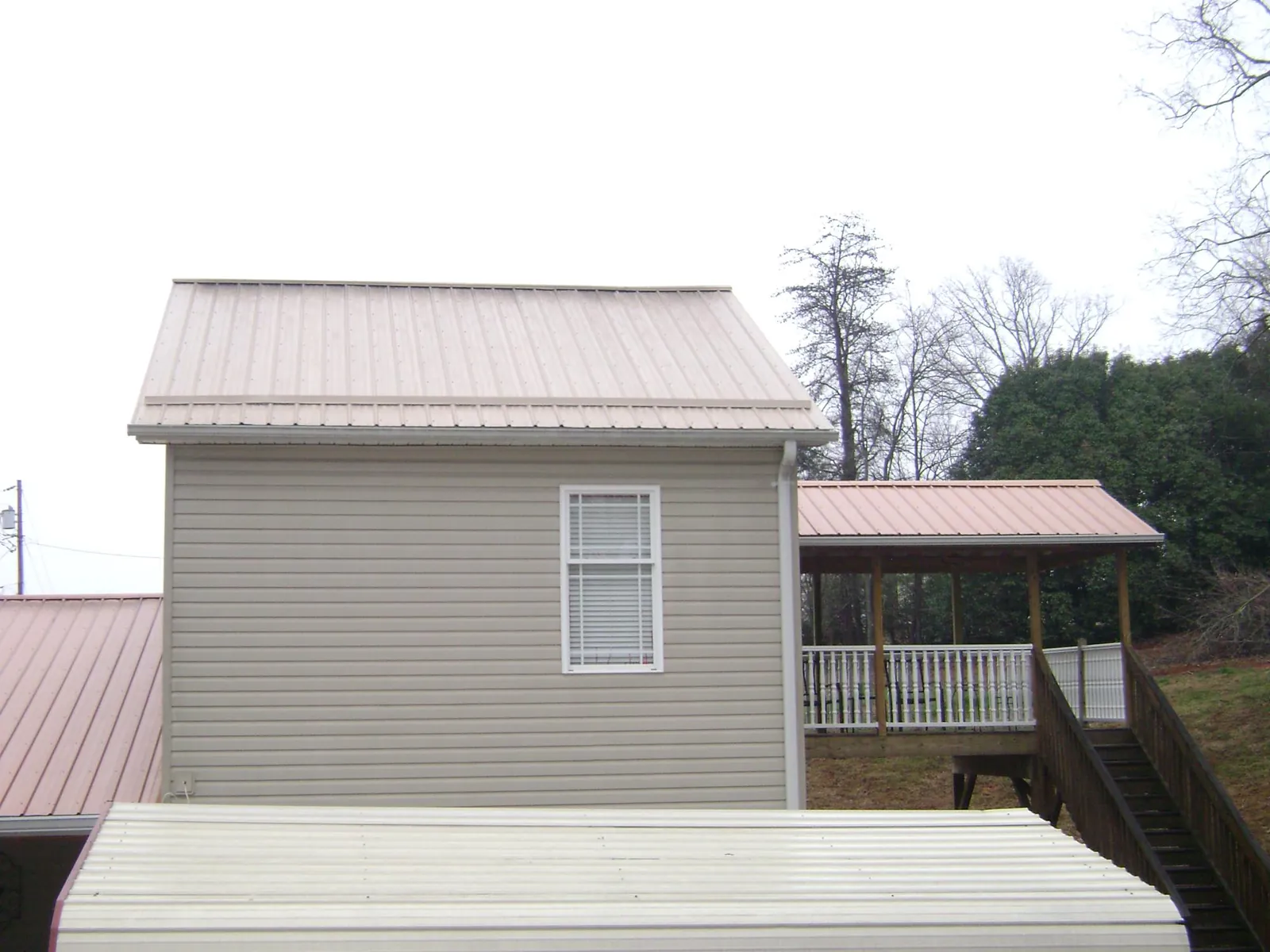 Tan metal roofs on a two story addition and attached porch, from a Roof Replacement job in Cantrall